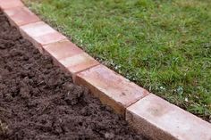 there is a patch of dirt next to the grass and some bricks that are laying on the ground