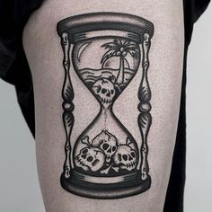 a man's thigh with an hourglass tattoo on it and skulls in the sand