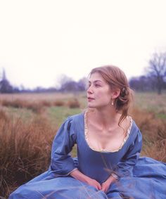 a woman in a blue dress sitting on the ground with her hands behind her back