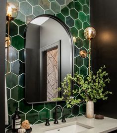 a bathroom sink with a mirror and vase on it's side next to a green tiled wall