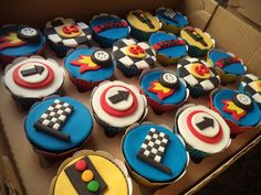 cupcakes decorated in the shape of cars and racing symbols are displayed on a cardboard box