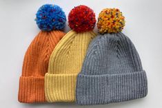 three knitted hats with multi colored pom poms on top of each other