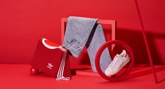 a pair of white adidas sneakers sitting on top of a red chair next to jeans