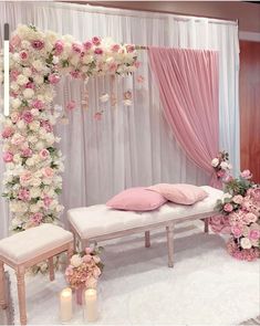 a pink and white wedding setup with flowers on the wall, candles in vases