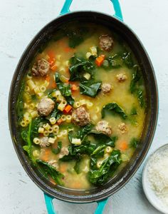 a pot filled with meatballs, pasta and spinach soup next to a spoon