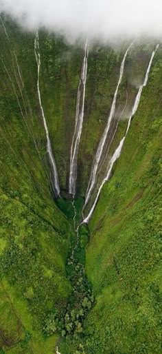 an aerial view of a waterfall in the middle of a lush green field with trees