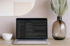 a laptop computer sitting on top of a wooden desk next to a vase with a plant