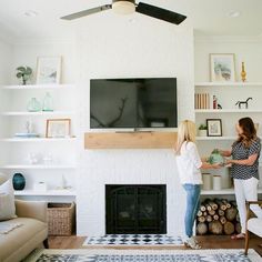 two women standing next to each other in front of a tv on a white brick wall