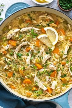 a pot filled with chicken noodle soup next to lemon wedges and parsley