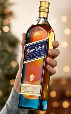 a person holding up a bottle of blue label whisky in front of a christmas tree