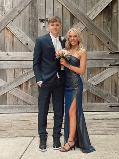 a young man and woman posing for a photo in front of a wooden fence with flowers