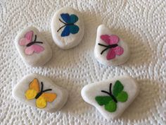 four painted rocks sitting on top of a white cloth covered tablecloth with butterfly designs