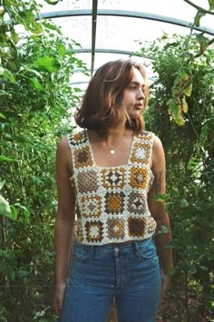 a woman is standing in the middle of a garden wearing jeans and a crocheted top