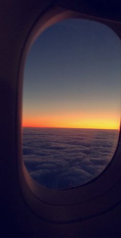 the view out an airplane window shows clouds below and in the distance, at sunset