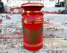 a red and gold painted mailbox sitting on the side of a stone wall next to steps