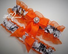 This adorable garter set is made of white True Timber Snowfall Satin Camo print and Orange Organza Trim. They are embellished with Orange satin bows, pearl and rhinestone brooch and matching ribbon. You have the option to have no charm added or choose between different charms to add that personal touch! Included in the set is a beautiful Keepsake garter as well as a Toss-away garter. These garters are made of quality fabric, lace and ribbons. Relaxed these garters measure 15 in. Stretched they m Camo Wedding Dress, Country Style Wedding Dresses, Camouflage Wedding, Prom Garters, Fall Wedding Color Schemes, Wedding Toasting Glasses, Garter Wedding, White Garters, Shabby Chic Flowers