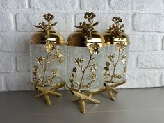 three glass vases with gold flowers on them sitting next to each other in front of a white brick wall