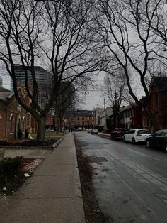 an empty street lined with parked cars and trees