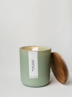 a green candle with a wooden lid sitting on a white surface next to a tag