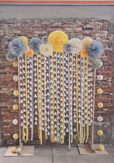 an arrangement of paper flowers and pinwheels on display in front of a brick wall