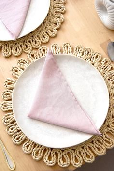 a place setting with pink napkins and silverware on a wooden tableclothed doily