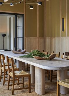 a dining room table with chairs and a bowl of greens on the table in front of it