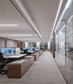 an office with rows of desks and computer screens on the wall in front of glass walls