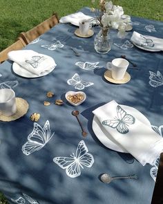 a blue table cloth with white butterflies on it and plates, cups, spoons and utensils