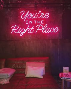 a neon sign that says you're in the right place on a wall above a couch