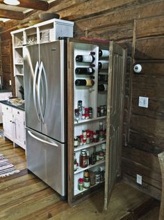 an open refrigerator in the middle of a room with wooden floors and walls, filled with bottles