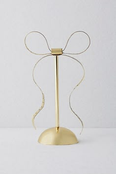 a gold candle holder with a bow on it's top and a white wall in the background