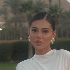 a woman wearing large gold earrings and a white top