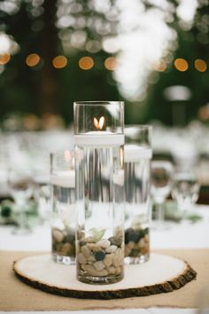 the table is set with candles, rocks and glass vases for centerpieces