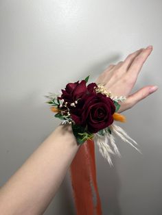 a woman's hand holding a red rose and feather corsage