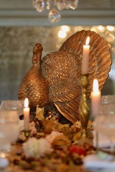 two turkey figurines sitting on top of a table surrounded by candles and flowers