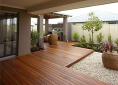 a wooden deck in the middle of a yard with plants and rocks on it, next to an outdoor kitchen