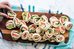 a wooden cutting board topped with lots of veggie wrapped in wrappers on top of a marble counter