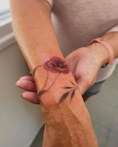 a woman's arm with a red flower tattoo on the left side of her wrist