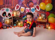 a little boy sitting on the floor in front of some balloons and decorations for his birthday