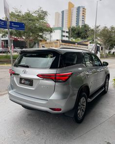 the rear end of a silver car parked in front of a street sign with buildings in the background