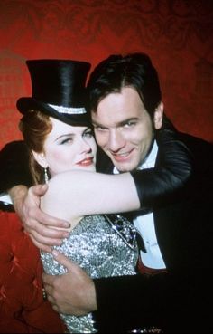 a man and woman hugging each other in front of a red wall wearing top hats