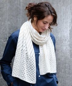 a woman wearing a white scarf and blue shirt standing in front of a gray wall