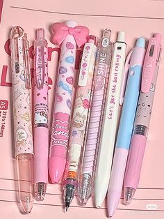 several different types of pens lined up on a pink surface with hello kitty stickers