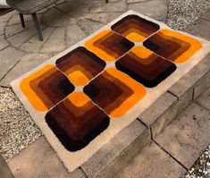 an orange and brown rug sitting on top of a stone floor next to a bench