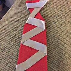 a red tie with white ribbons tied to it on a couch next to a person's feet