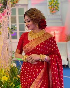 a woman in a red and gold sari standing next to a flower pot with flowers on it