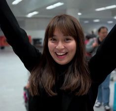 a woman is holding her arms up in the air and smiling at the camera with other people behind her