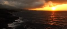 the sun is setting over the ocean with dark clouds in the sky and water below