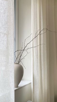 a vase sitting on top of a window sill next to a white drapes