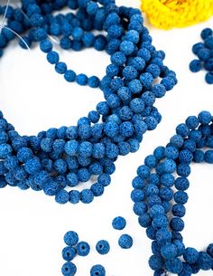 some blue beads are laying next to each other on a white surface with a yellow flower in the background